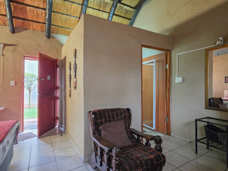 Bedroom featuring a rustic thatched roof with exposed rafters, tiled flooring, and direct access to an en-suite bathroom and exterior entrance.