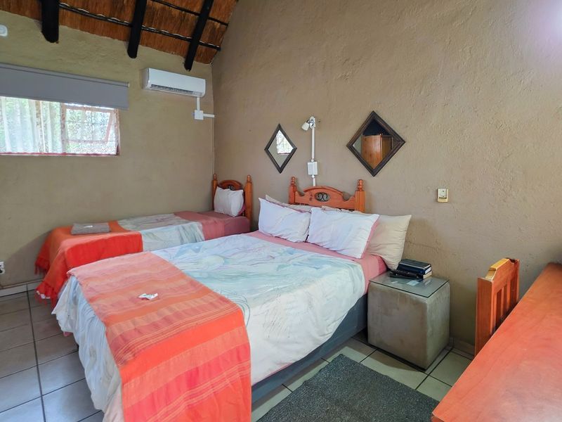 A bedroom featuring a traditional thatched roof with exposed timber rafters, tiled flooring, and a wall-mounted air conditioning unit.