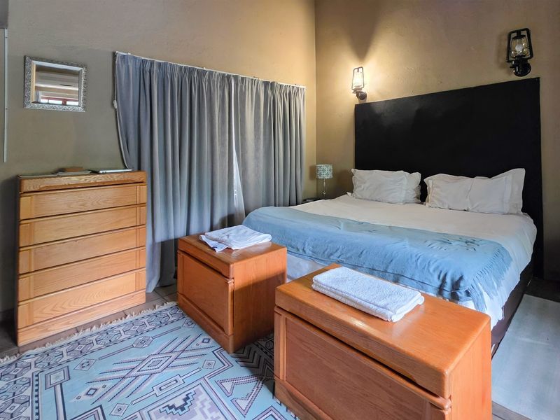 A cozy bedroom featuring neutral wall tones, built-in wall lighting, and window treatments, offering a comfortable and functional sleeping space.