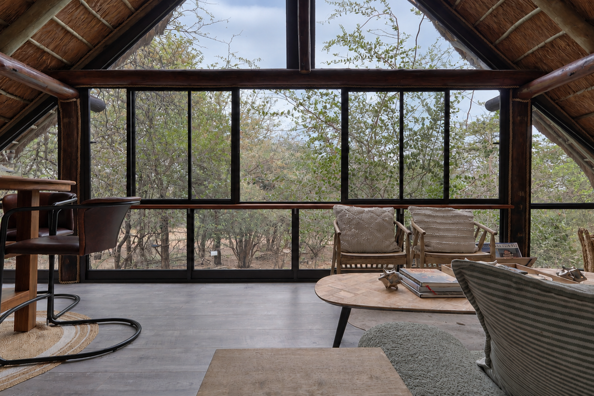 A bright living area featuring a high vaulted thatched ceiling with exposed timber beams and expansive windows offering natural views.