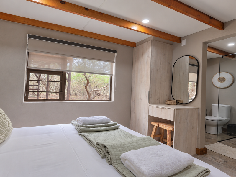 A well-appointed bedroom featuring exposed timber ceiling beams, a built-in vanity with wardrobe, and an integrated en-suite bathroom with a modern glass shower enclosure.