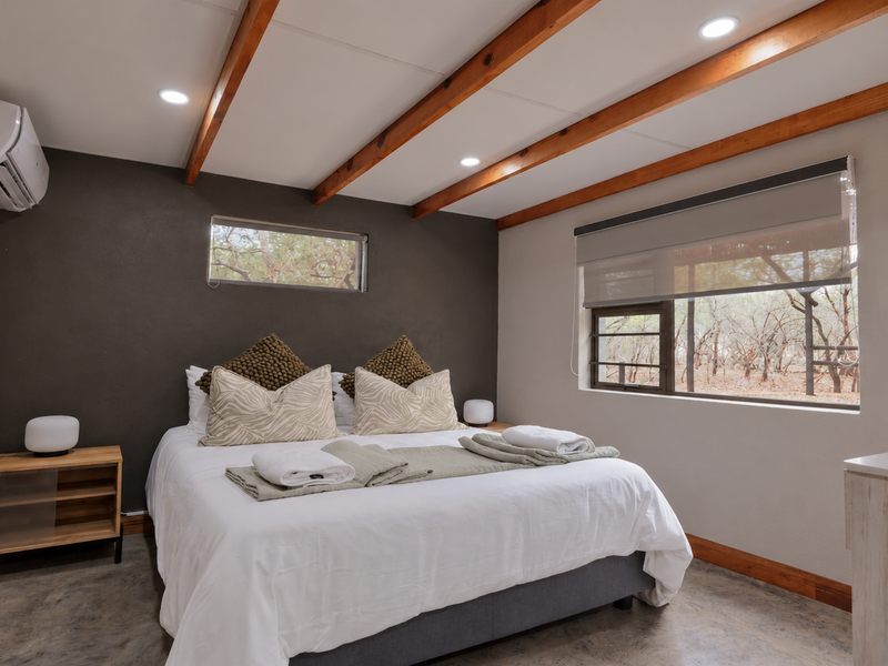A well-maintained bedroom featuring exposed timber ceiling beams, polished concrete floors, and a split-system air conditioner, offering a modern and comfortable living space.
