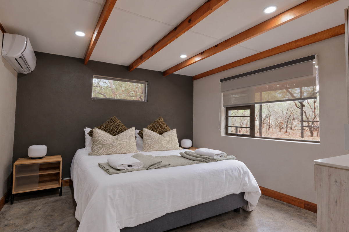 A well-maintained bedroom featuring exposed timber ceiling beams, polished concrete floors, and a split-system air conditioner, offering a modern and comfortable living space.