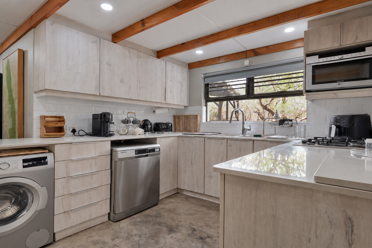 Modern kitchen featuring light wood-look cabinetry, stone countertops, subway tile backsplash, exposed timber ceiling beams, and integrated appliances with polished concrete flooring.