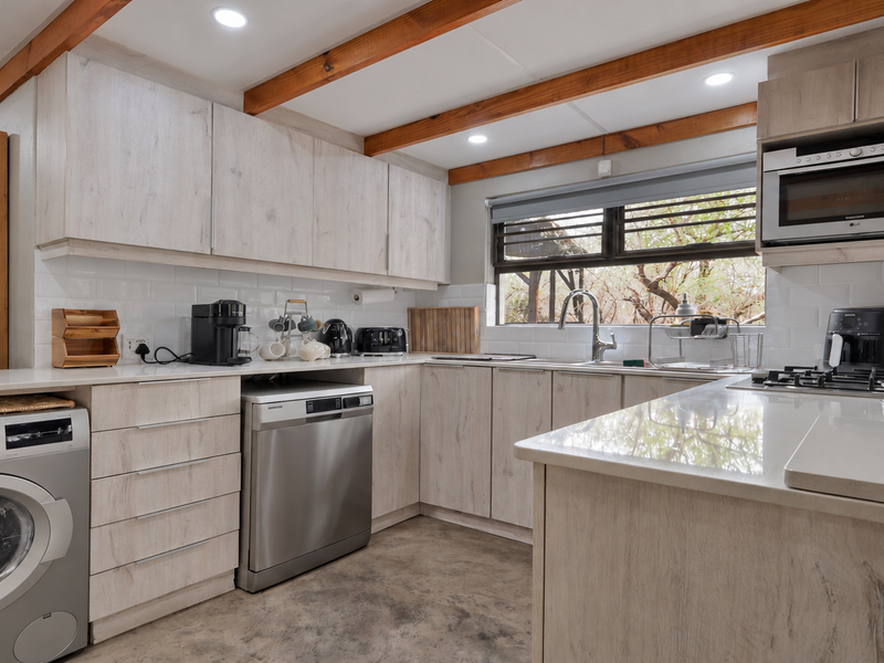 Modern kitchen featuring light wood-look cabinetry, stone countertops, subway tile backsplash, exposed timber ceiling beams, and integrated appliances with polished concrete flooring.