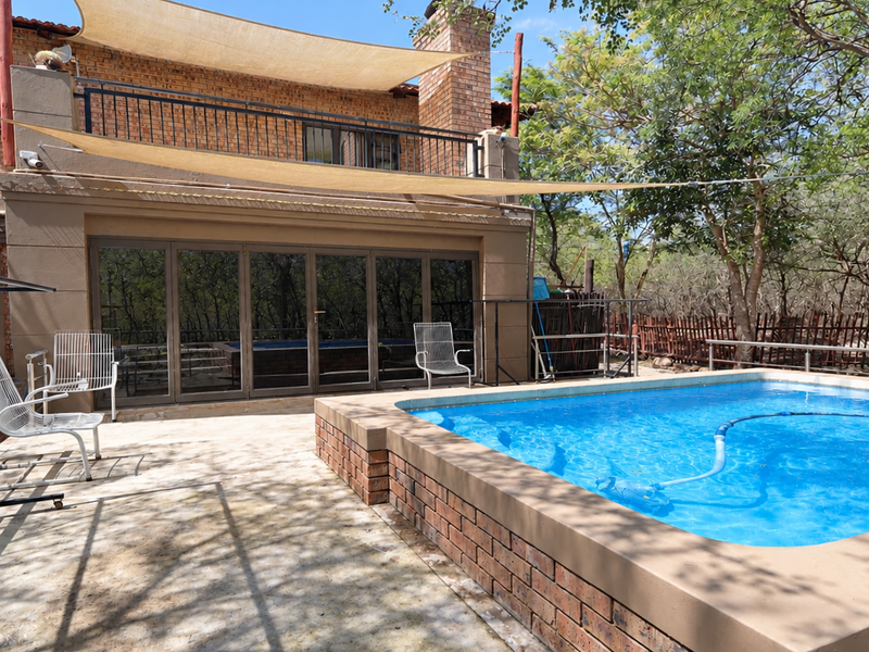 Outdoor pool area featuring a raised brick-edged swimming pool, shade sail, and large folding glass doors leading into the home.