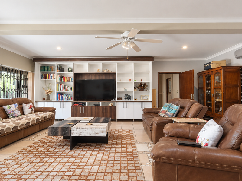 Spacious living room featuring a large built-in media wall with shelving, tiled flooring, ceiling fan, and split-system air conditioning.
