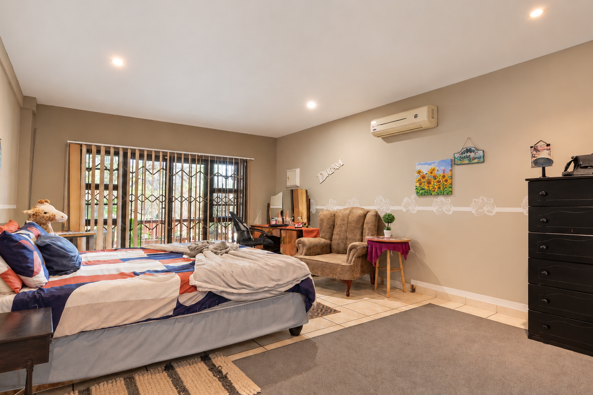 Spacious bedroom featuring tiled flooring, a split-system air conditioner, and large sliding glass doors with security gates providing access to the exterior.