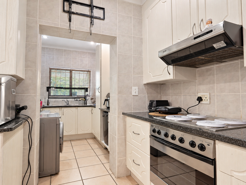 A functional kitchen featuring light-toned cabinetry, granite countertops, a built-in oven with hob, and a separate scullery area with additional sink and storage.