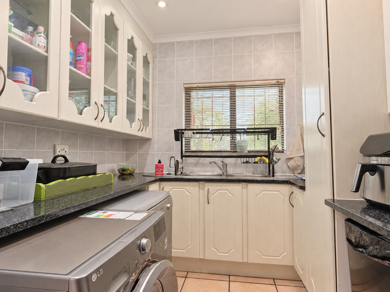 A functional scullery featuring ample built-in cabinetry, granite countertops, a double sink, and tiled finishes, providing a dedicated space for laundry and prep.
