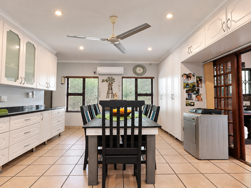 Spacious open-plan kitchen and dining area featuring white cabinetry, granite countertops, tiled flooring, and direct access to an adjacent utility space through sliding doors.