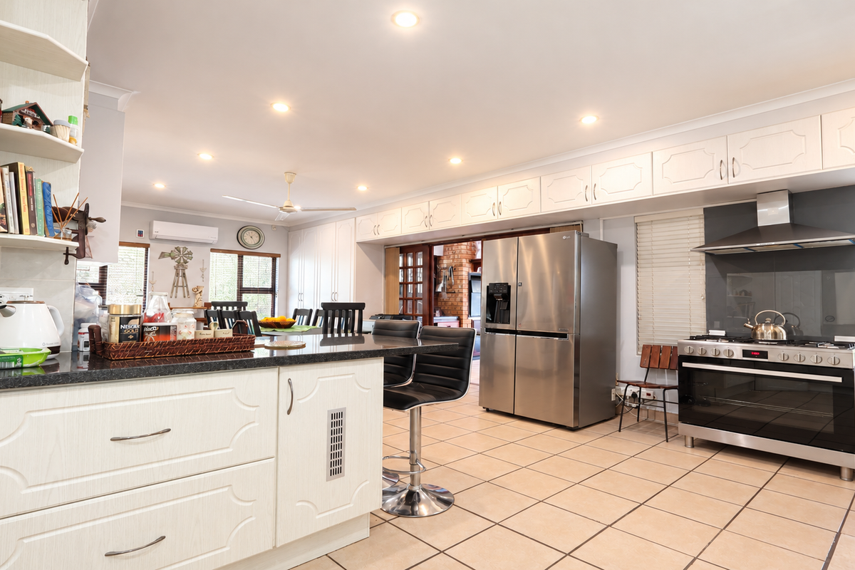 Spacious kitchen featuring granite countertops, ample built-in cabinetry, stainless steel gas stove with extractor fan, and tiled flooring throughout.