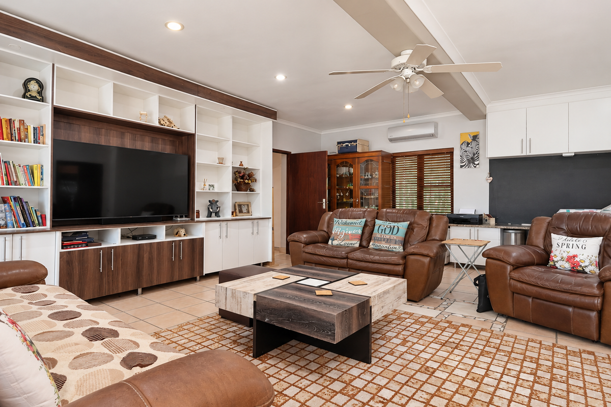 Spacious living room featuring a large built-in media and shelving unit, tiled flooring, ceiling fan, and split-system air conditioning for climate control.