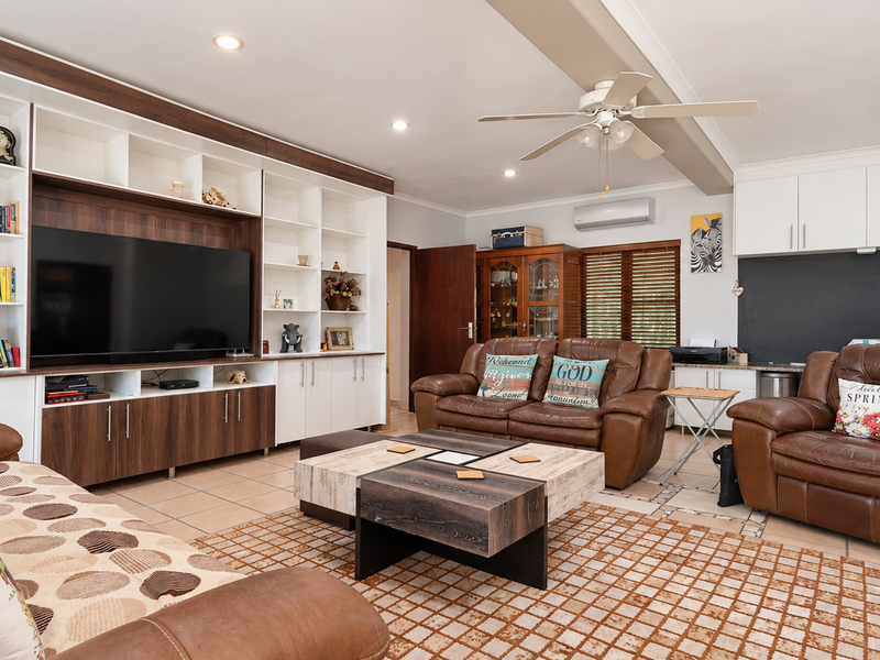 Spacious living room featuring a large built-in media and shelving unit, tiled flooring, ceiling fan, and split-system air conditioning for climate control.