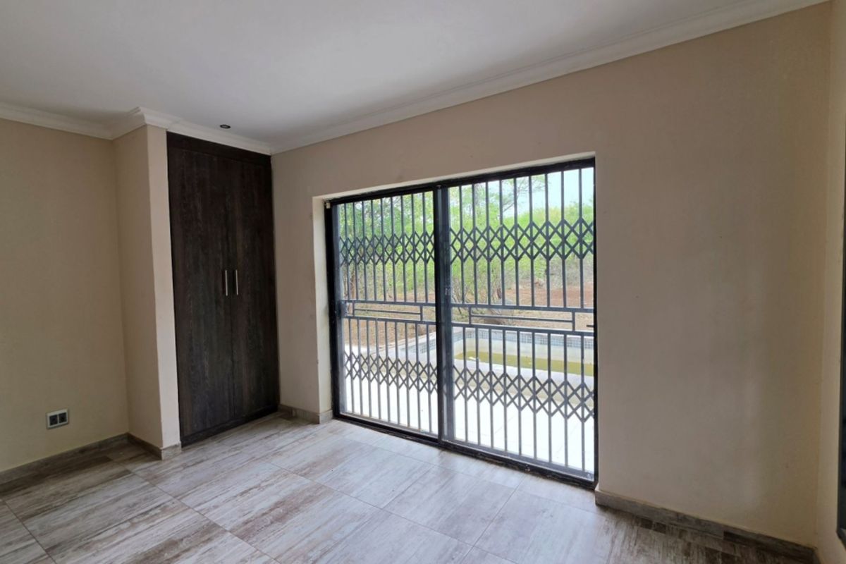 A bright, empty bedroom featuring tiled flooring, a built-in wardrobe, and a sliding glass door with a security gate leading to the exterior.