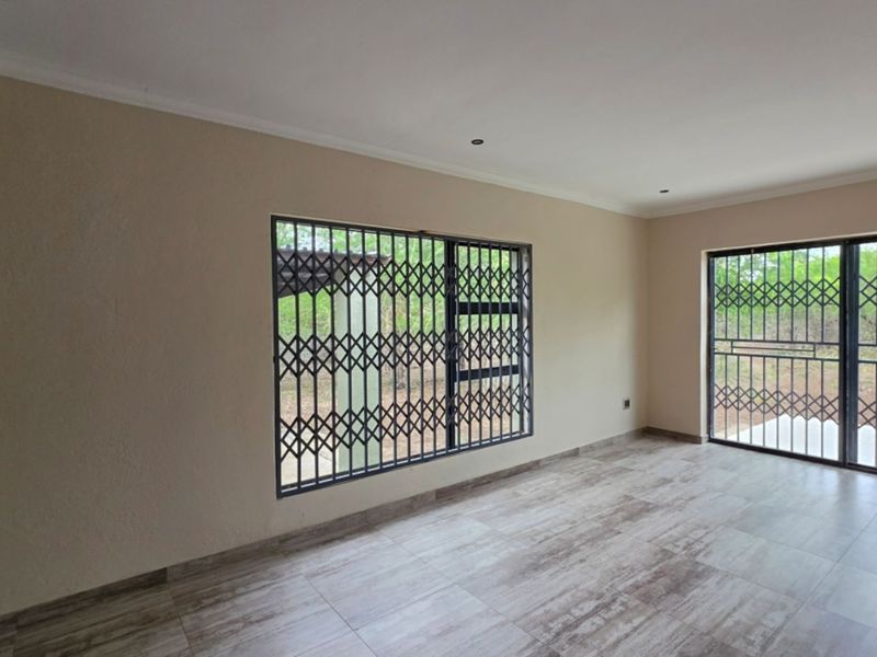 A bright, empty living area featuring modern wood-look tiled flooring, recessed lighting, and security gates on the windows and sliding door.