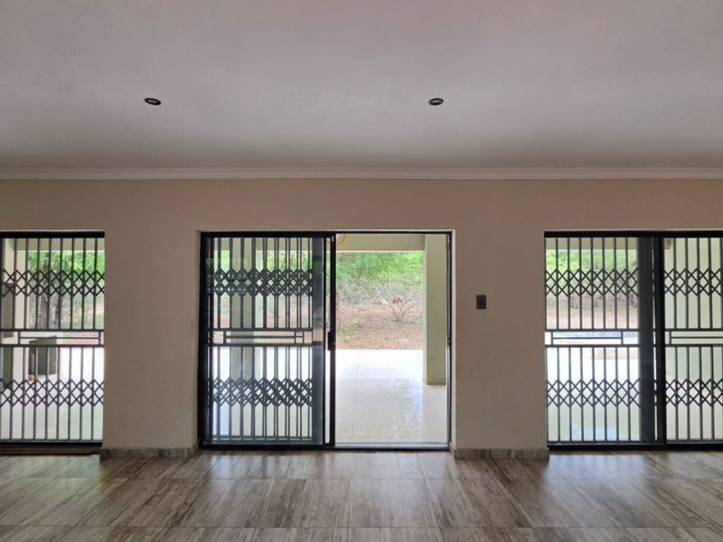 Spacious living area featuring tiled flooring, recessed downlights, and multiple sliding glass doors with security gates leading to an outdoor patio area.