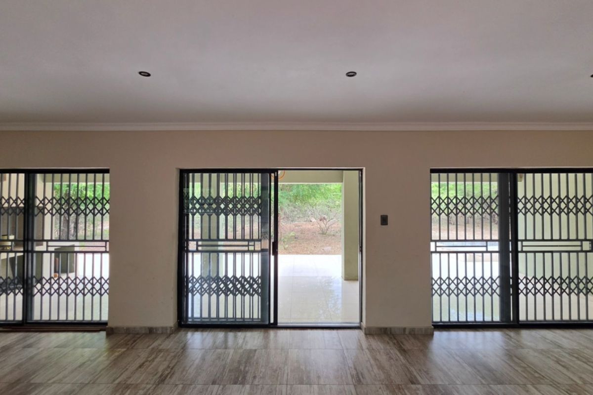 Spacious living area featuring tiled flooring, recessed downlights, and multiple sliding glass doors with security gates leading to an outdoor patio area.