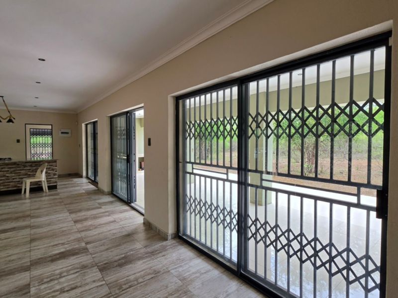 Spacious open-plan living area featuring tiled floors, recessed lighting, and large sliding glass doors with security gates leading to the exterior.