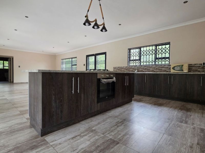 Spacious open-plan kitchen featuring a central island with built-in oven, stone countertops, and modern tiled flooring, offering a clean and functional layout.