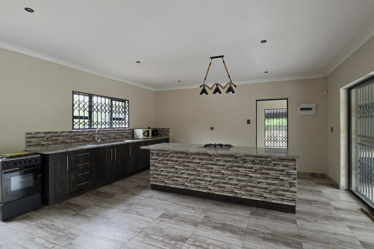 Modern kitchen featuring a central island with stone veneer finish, granite countertops, built-in stove, and tiled flooring, offering a spacious and functional layout.