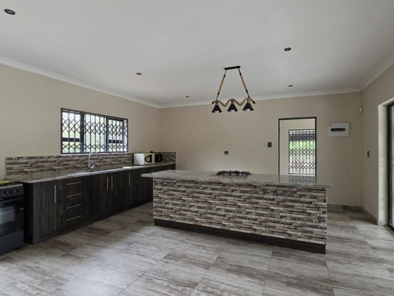 Modern kitchen featuring a central island with stone veneer finish, granite countertops, built-in stove, and tiled flooring, offering a spacious and functional layout.