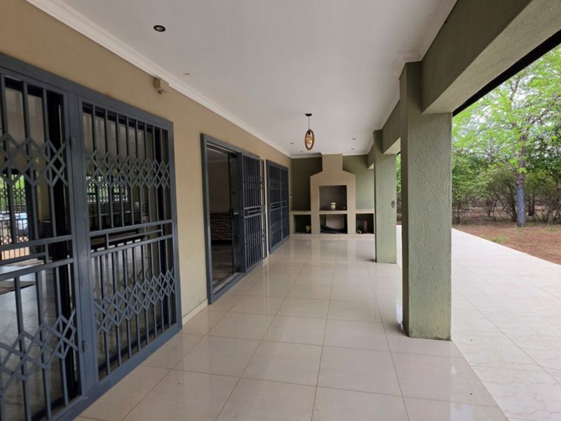 Spacious covered patio featuring tiled flooring, built-in braai, and secure access points, overlooking a natural garden setting.