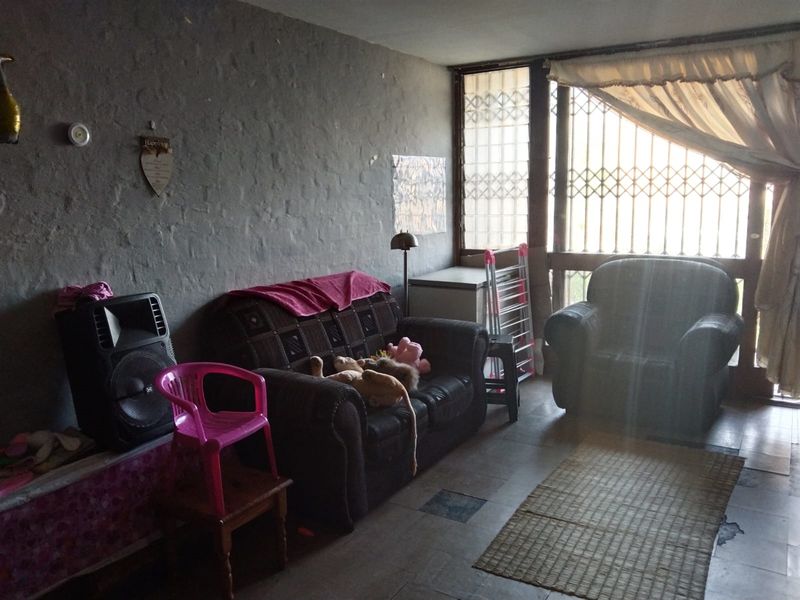 A living room area featuring textured walls, tiled flooring, and a large window secured with a metal security gate.
