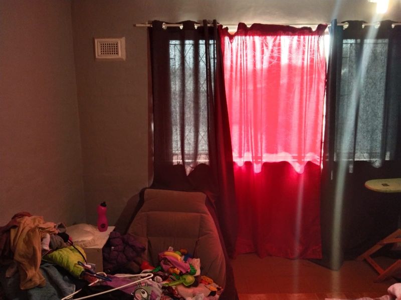 A bedroom featuring security bars on the window and a wall ventilation unit, requiring cosmetic updates to improve the overall aesthetic.