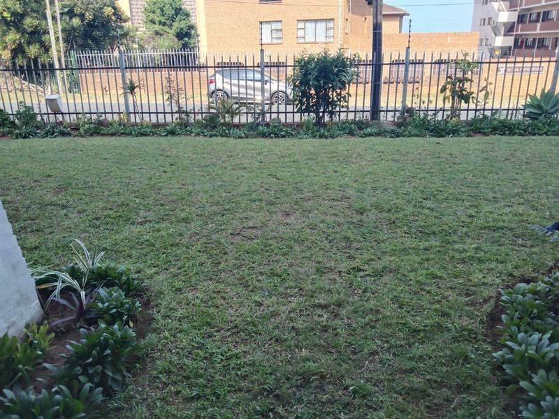 A well-maintained private garden area featuring a manicured lawn and secure metal perimeter fencing with integrated electric security wires.