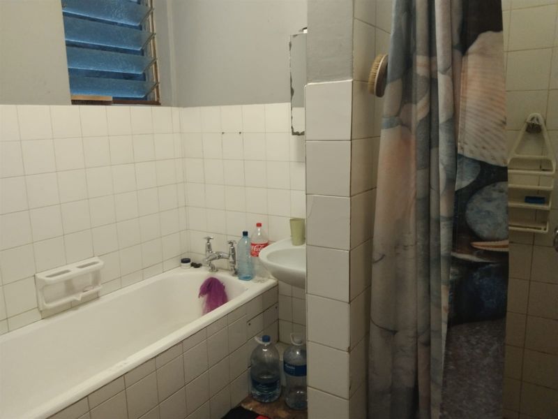 A functional bathroom featuring a bathtub, basin, and tiled walls with a louvered window for ventilation.