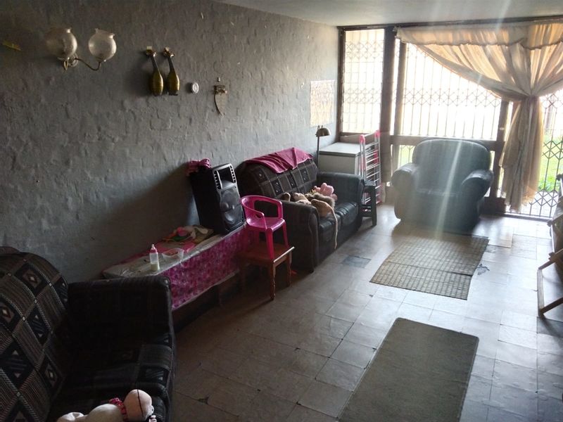 A living room area featuring tiled flooring, textured walls, and a large window with a security gate, offering potential for modernization.