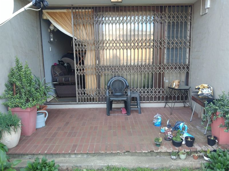 A covered patio area featuring brick paving, a sliding glass door with a security gate, and direct access to the interior living space.