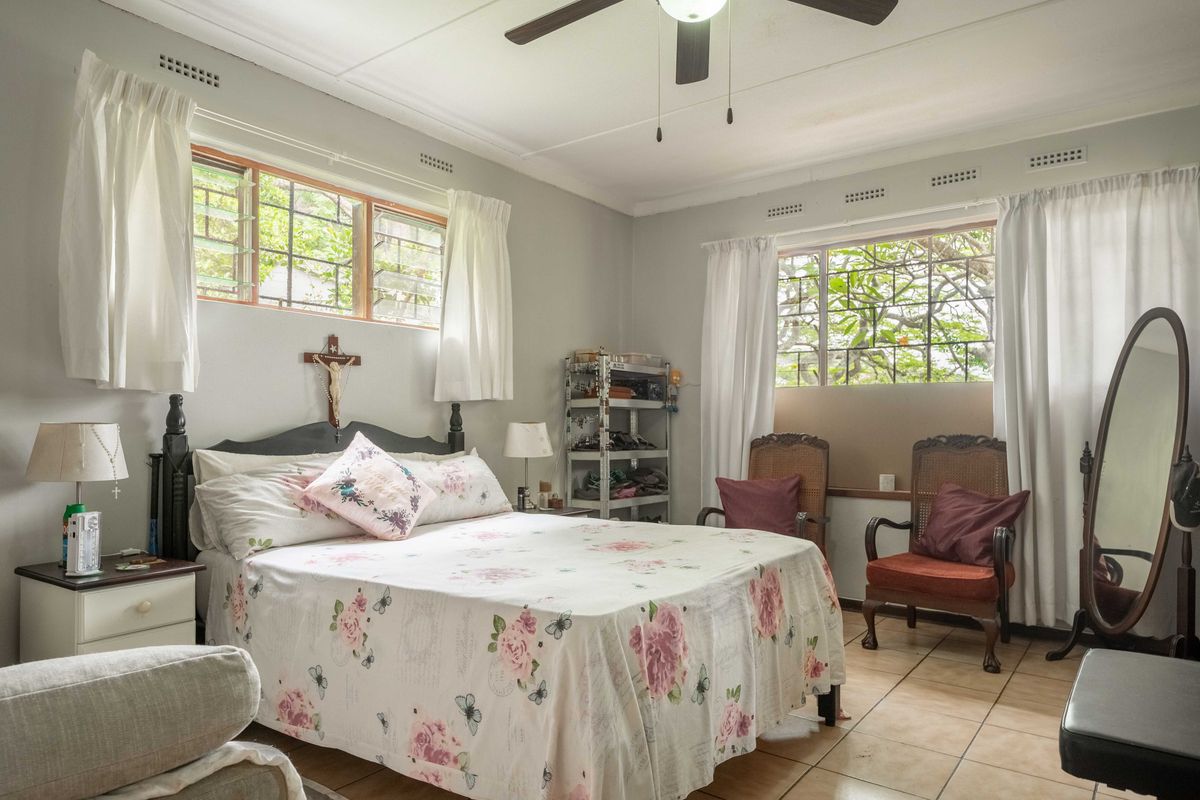 A spacious bedroom featuring tiled flooring, a ceiling fan, and large steel-framed windows that provide ample natural light.