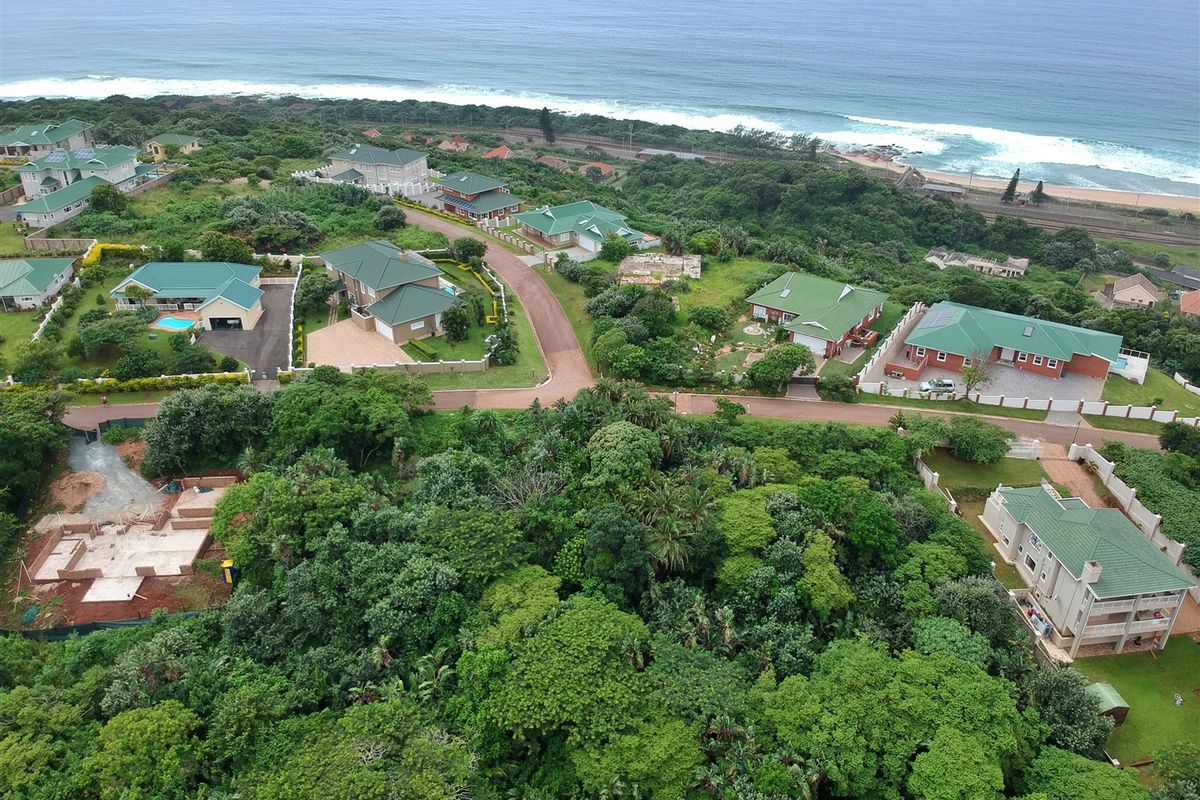 An aerial view of a coastal residential estate featuring established homes, lush green vegetation, and proximity to the ocean.