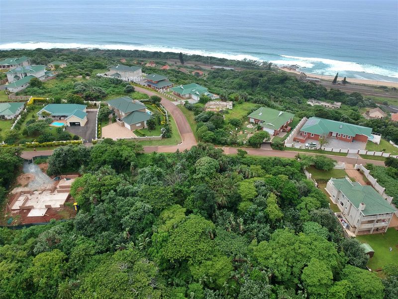An aerial view of a coastal residential estate featuring established homes, lush green vegetation, and proximity to the ocean.