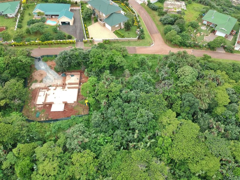 Aerial view of a residential vacant land plot featuring a concrete foundation and brickwork in progress, surrounded by established trees and neighborhood infrastructure.
