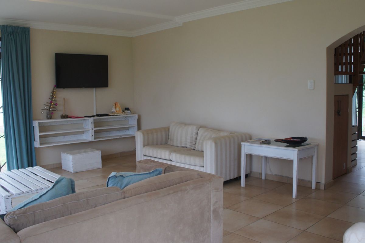 Spacious living room featuring tiled flooring, an arched entryway leading to a staircase, and direct access to the outdoor area through a security gate.