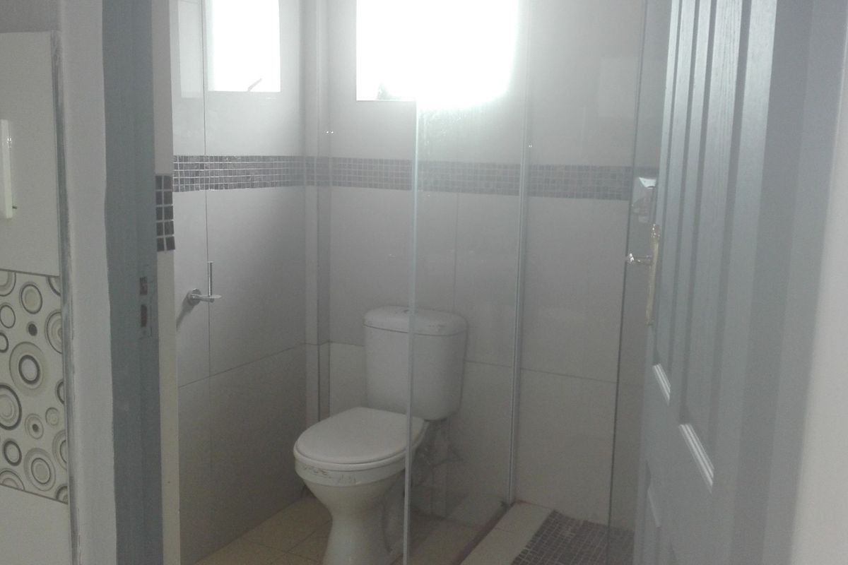 A compact bathroom featuring a toilet, glass shower enclosure, and decorative mosaic tile accents on the walls.