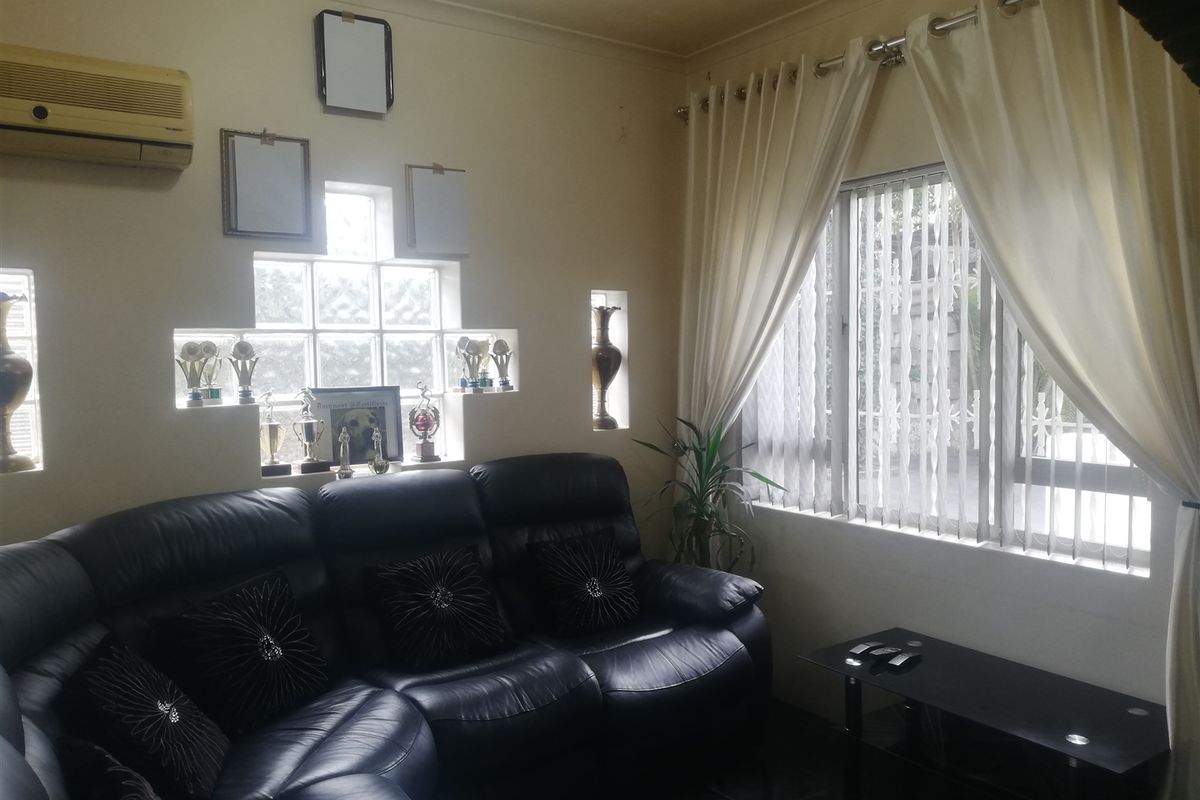 A living room featuring a glass block feature window, vertical blinds, and a wall-mounted air conditioning unit.