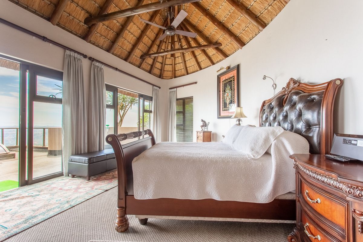 Spacious bedroom featuring a high vaulted thatched ceiling with exposed timber rafters, ceiling fan, and large sliding glass doors leading to an outdoor area.