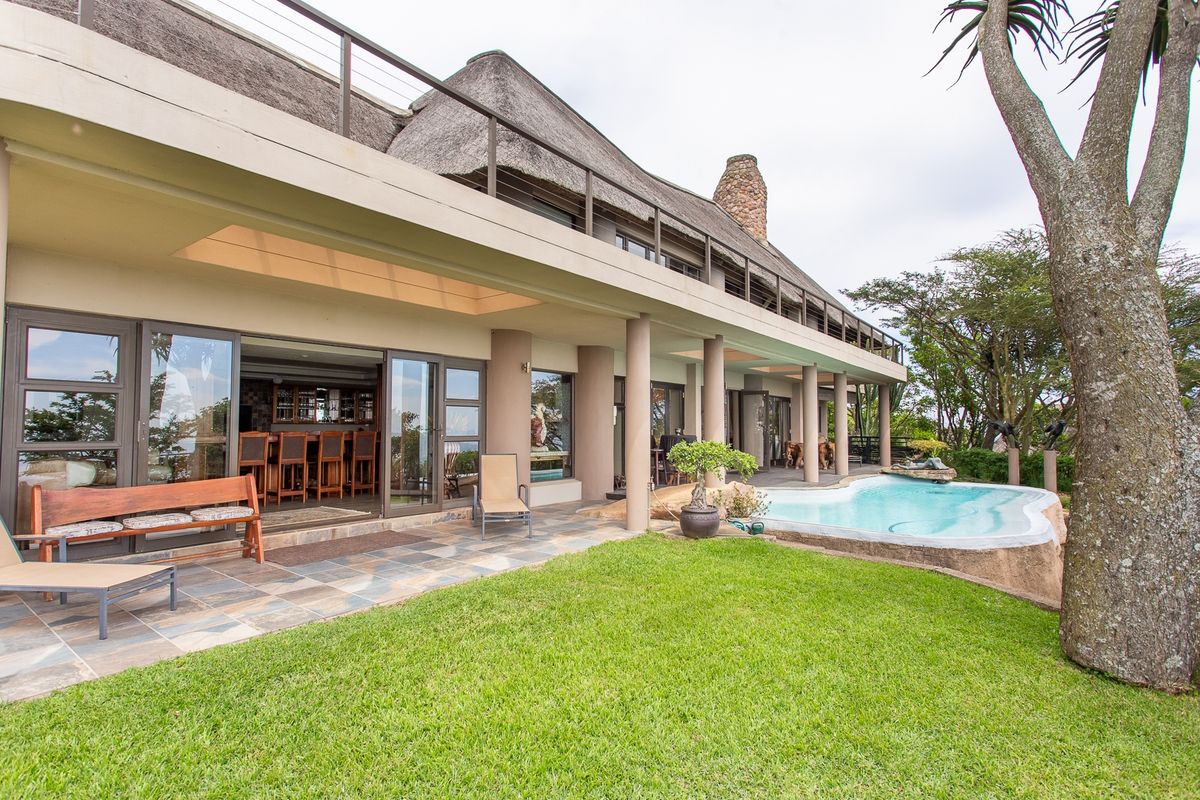 Rear exterior view featuring a thatched roof house, a swimming pool, and a spacious covered patio with sliding glass doors.