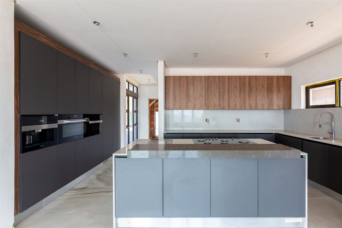 Modern kitchen featuring dark cabinetry, wood-grain upper cabinets, a central island with a built-in cooktop, and integrated appliances.