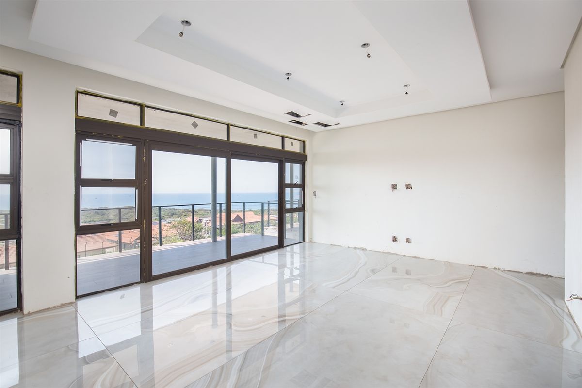 Spacious living area featuring large sliding glass doors, polished marble-look floor tiles, and a recessed ceiling, offering expansive coastal views.