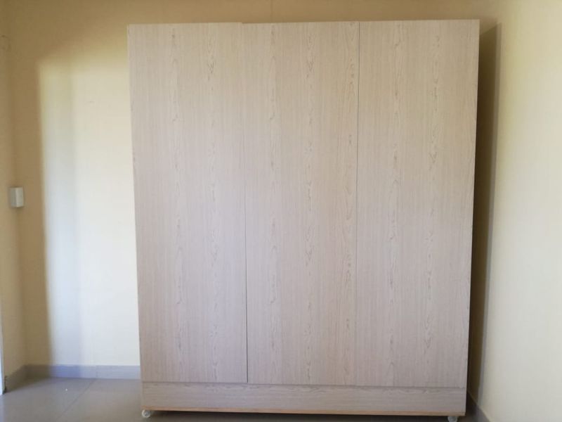 A bedroom space featuring a light wood-finish built-in wardrobe with three doors.