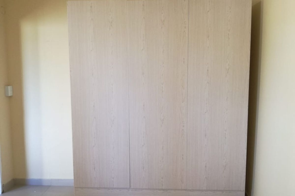 A bedroom space featuring a light wood-finish built-in wardrobe with three doors.