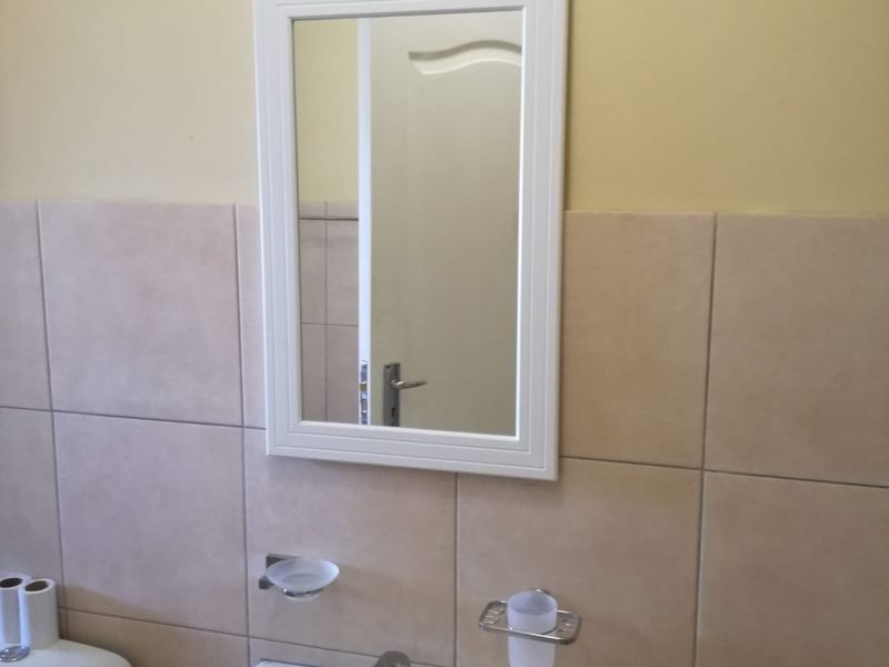 A functional bathroom featuring a wall-mounted basin with chrome mixer tap, tiled walls, and a framed mirror.