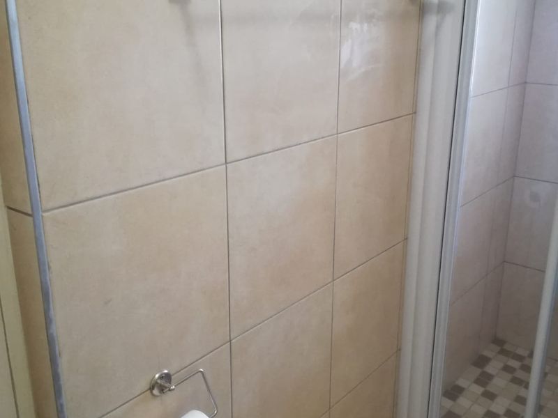 A functional bathroom featuring neutral wall tiles, a glass shower enclosure, and fixed chrome bathroom accessories.