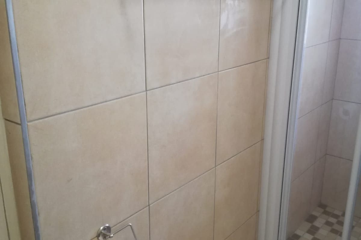 A functional bathroom featuring neutral wall tiles, a glass shower enclosure, and fixed chrome bathroom accessories.