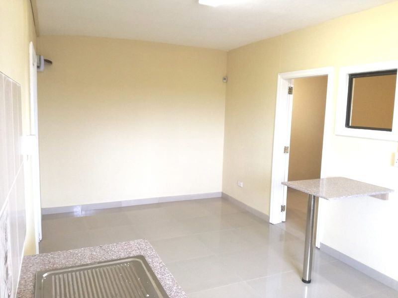 A clean, empty kitchen area featuring tiled flooring, a stainless steel sink, and a built-in breakfast bar with granite countertop.